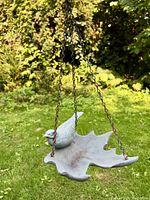 Hanging plastic bird bath with a bird figurine on a leaf-shaped tray against a garden background.