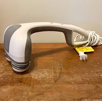 Full side view of the white and gray handheld electric massager on wood surface, showing the ergonomic handle and massage head with dual nodes.