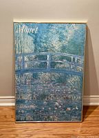 Frontal view of the Monet art wall hanging showing the painted bridge and surrounding water lilies with the signatures at top and bottom corners.