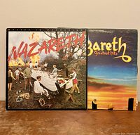 Front covers of two Nazareth vinyl LP records: "Malice in Wonderland" and "Greatest Hits". "Malice in Wonderland" cover shows an outdoor scene with people and fire, "Greatest Hits" cover shows sunset artwork with the band's name.