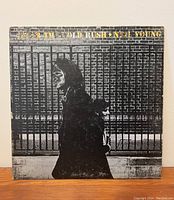 Front cover of Neil Young After the Gold Rush vinyl album featuring monochrome image of two figures walking past wrought iron fence, title in gold foil letters.