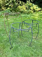 Photo showing set of three outdoor metal plant stands, two dark blue and one brown, positioned on grass outdoors.