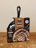 Front view of small cast iron skillet in box showing cinnamon roll image and product description