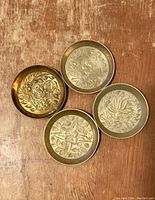 Top down view of all four round vintage brass coasters showing different floral and botanical etched designs on their surfaces.