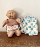 Front view of vintage Cabbage Patch doll seated wearing a floral cloth diaper with three new diapers laid next to it