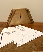 Wooden lap harp zither with music sheets laid in front, showing overall item with music materials.