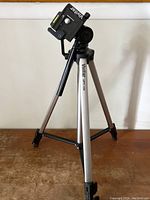 Full view of Vivitar VPT-120 tripod showing extendable silver legs with black locks and the pan-tilt head with handle, placed on wooden surface against white background.