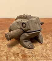 Side view of the carved wooden frog with rasp scraper attached to the side, showing the textured ridges and carved details.