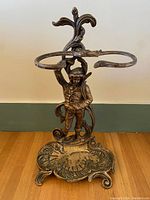 Front view of antique metal umbrella stand showing figurine and umbrella rings