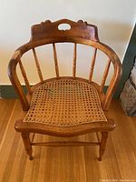 Front view of antique wooden barrel back chair showing curved spindle back and damaged cane seat.