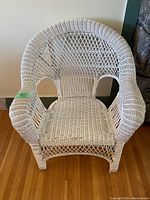 Front view of white wicker armchair showing woven seat and detailed arched backrest with fan pattern, slight wear noted on left armrest