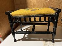 Front and side angle view of antique wooden footstool with black painted wood frame and needlepoint seat featuring a frog design on mustard yellow background.
