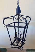 Full view of black metal vintage lantern pendant chandelier with six faux candle lights and leaf scroll details.