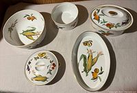Five porcelain dishes with fruit motifs and gold trim arranged together on a white surface seen from above.