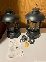 Pair of hunter green hurricane lanterns with accessories on white surface
