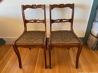 Front view of two matching vintage wooden occasional chairs with carved backs and green patterned upholstered seats, placed side by side.