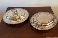 Pair of silver plate serving dishes with lids placed side by side on wooden table
