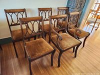 Set of six vintage dining chairs showing front view with one captain's chair and five armless chairs. Gold velvet upholstery visible, wooden carved backs and legs.
