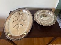 Top view of an oval silver plated meat platter and round stemmed silver candy dish side by side on a wooden surface