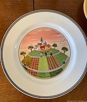 Front of plate showing colorful countryside farm village scene illustration with houses, fields, trees, and people.