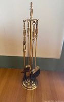Full view of vintage brass fireplace tool set on round base including poker, tongs, shovel, and broom.