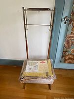Full front view of vintage clothes valet stand with packaged closet organizer on upholstered seat.