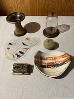 All six vintage decorative items arranged on a table, showing the candle holder, glass globe, cloche with base, pottery dish, painted glass plate, and brass stamp box.