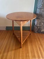 Full front view of the pine round side table showing the top and triangular base with lower shelf.