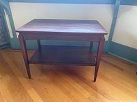 Front view of the vintage wooden side table showing rectangular top, tapered legs and bottom shelf.