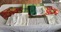 Overview photo of all linens laid out on table showing colorful table runner with abstract circular design, large green cloth, and stacks of white napkins.