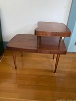Side view of the two-tier wooden step table showing the larger bottom tier, smaller elevated top tier, and tapered legs with brass-colored caps.