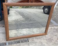 Full view of rectangular vintage walnut mirror, showing wood frame and reflective surface outdoors.