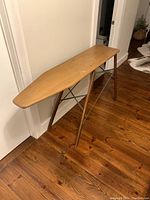 Side view of the antique wooden ironing board showing wooden top and legs on a hardwood floor.