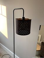 Side view of Umbra black metal floor lamp with perforated black shade showing scallop pattern and gold interior.