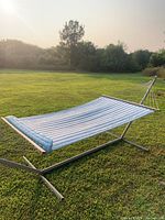Full side view of hammock setup in a grassy outdoor area under sunlight showing the metal frame and fabric surface.