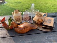 Photo showing variety of household articles including vases, trays, pictures, and figurines arranged on an outdoor wood surface