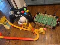 Overview of lot including Mario Kart Hot Wheels track, inflatable game controller, puzzle, globe night light, and tabletop soccer game on a wooden floor.