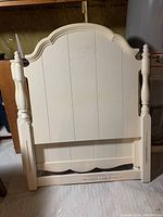 White wooden headboard with turned posts and paneled center, classic design with curved top molding