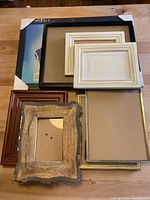 Photo showing eight various picture frames in different shapes and materials arranged on a wooden surface.