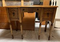 Front view of vintage wooden dressing table showing turned legs, three drawers with decorative carved panels and metal pull handles.
