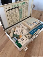 Open vintage first aid kit showing varied contents inside including safety pins, absorbent cotton, gauze bandages, and splints.