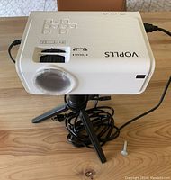 Top-down angled view showing projector with lens cap on and tripod attached on a table.