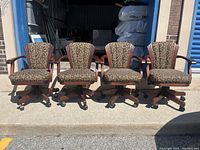 Full view of all four classic gaming chairs arranged side by side, showing floral upholstery and wooden frame with caster wheels.