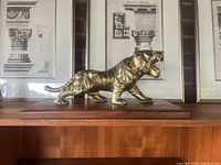 Full side view of brass tiger sculpture on teakwood base with architectural prints in background