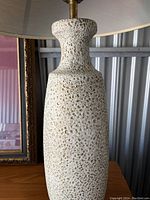 Close up front view of lamp showing heavily textured creamy white glazed ceramic surface with small indentations.