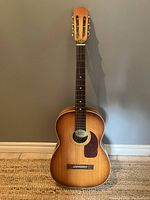 Front view of the Suzuki junior size acoustic guitar showing full body and fretboard against a wall.