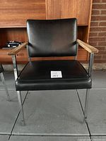 Front view of the vintage guest chair showing black vinyl seat and back, chrome frame, and walnut armrests.