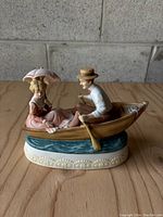 Front view of the porcelain music box figure featuring a man rowing a boat and a woman holding a parasol while seated.