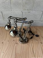 Two chrome desk work lamps with articulated arms and heavy round bases placed on wooden floor, photographed from an angle.