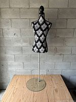 Full view of black and white female dress form mannequin with damask pattern, metal stand, and glass base.